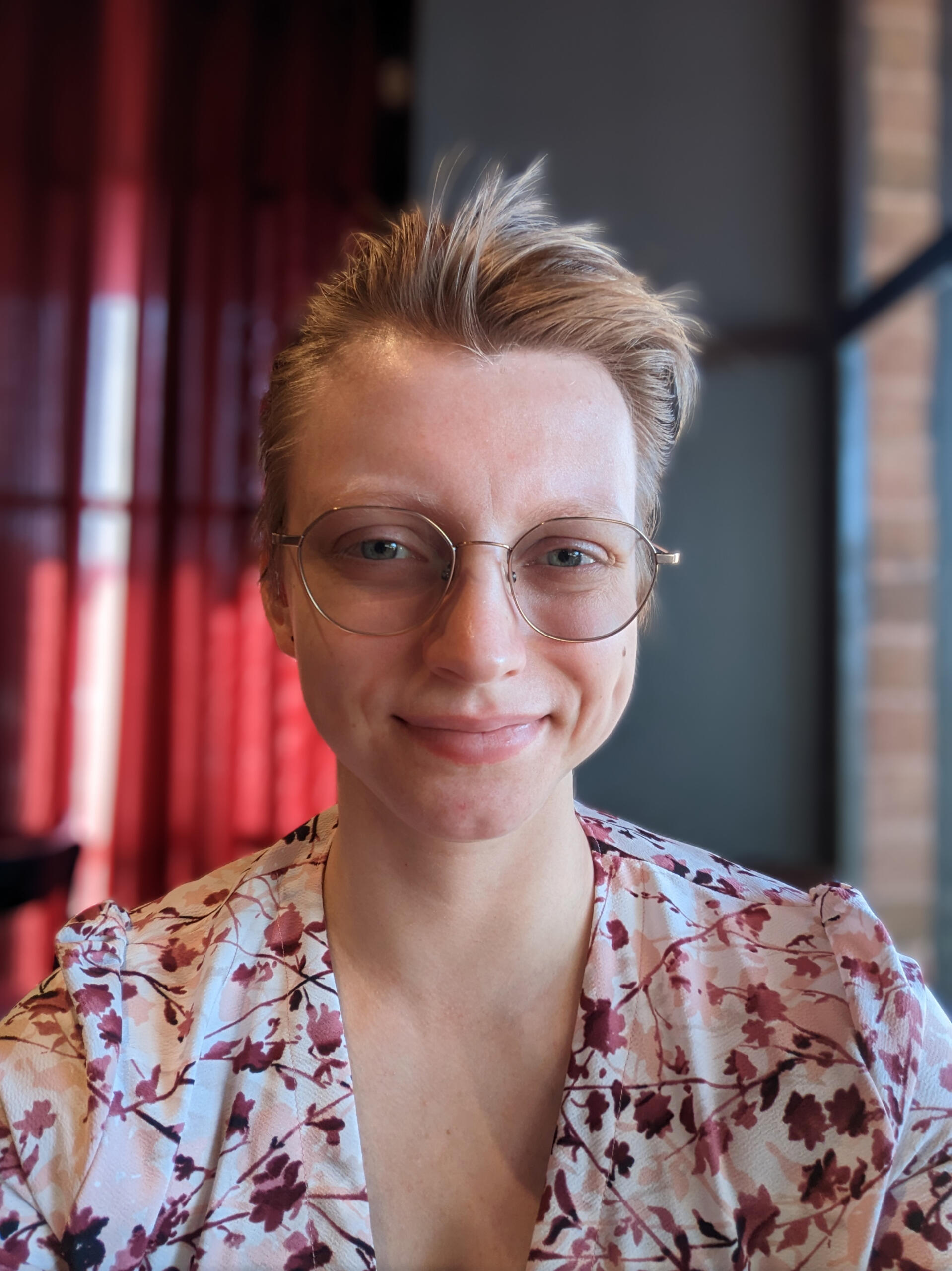 Image of a young white person with short blond hair and glasses. They are smiling.